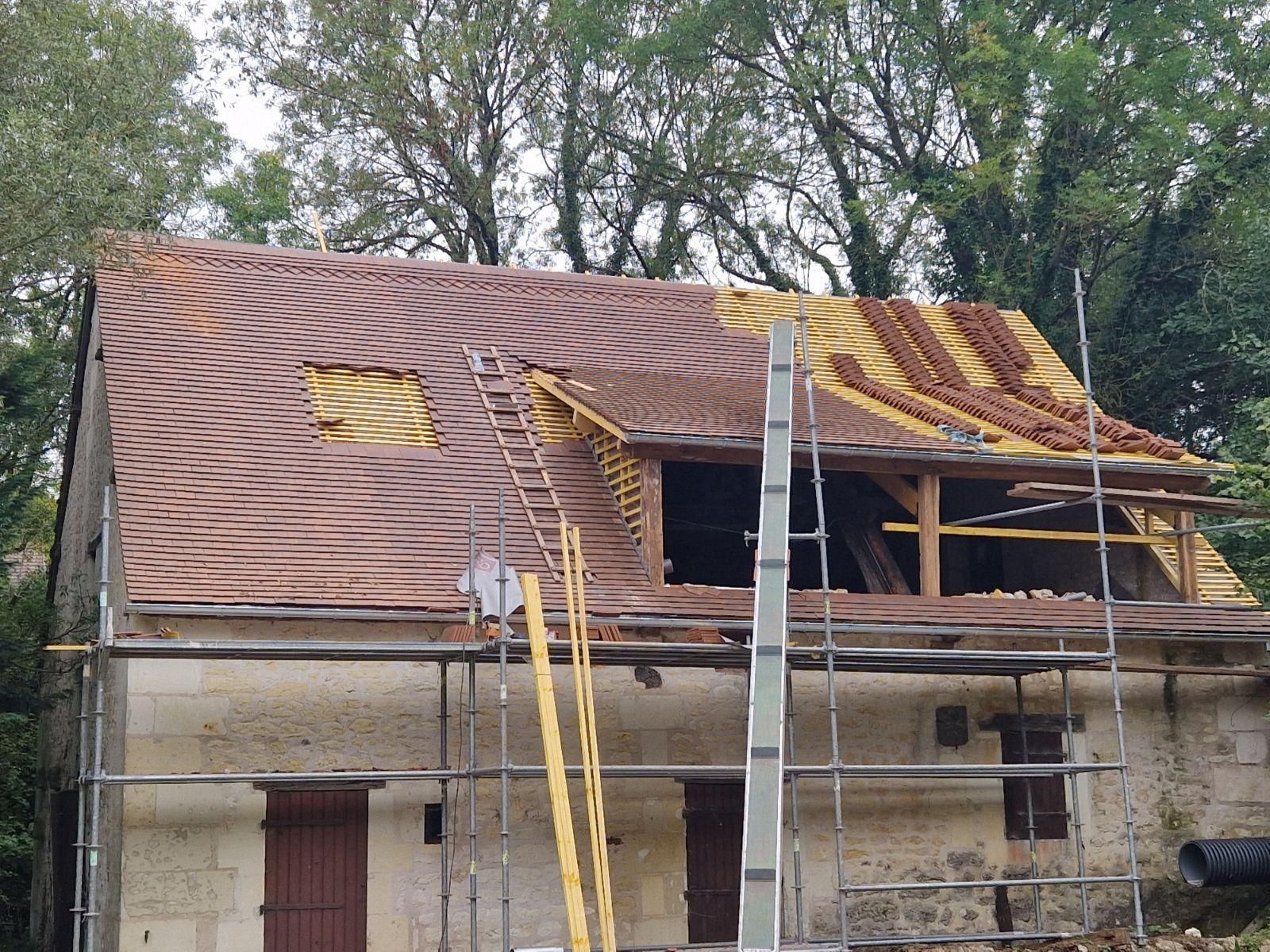 Toiture d'un bâtiment en pierre en cours de rénovation, partiellement recouverte de tuiles. 
