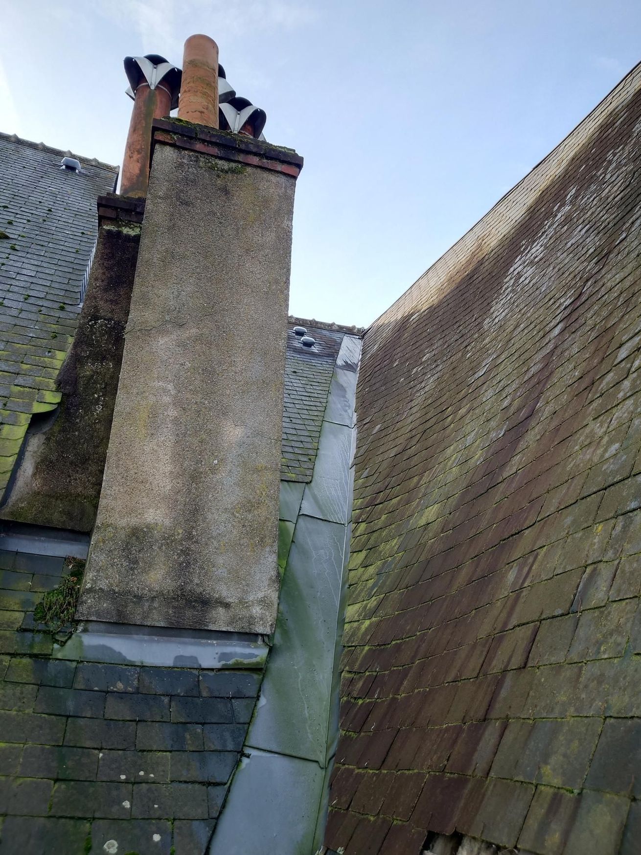 Cheminée sur un toit d'ardoise avec mousse et gouttière visibles. 