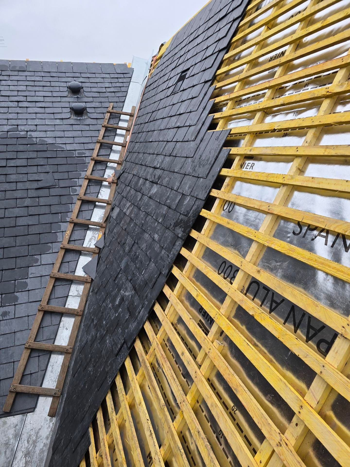 Toiture partiellement recouverte de bardeaux et ardoises noires.