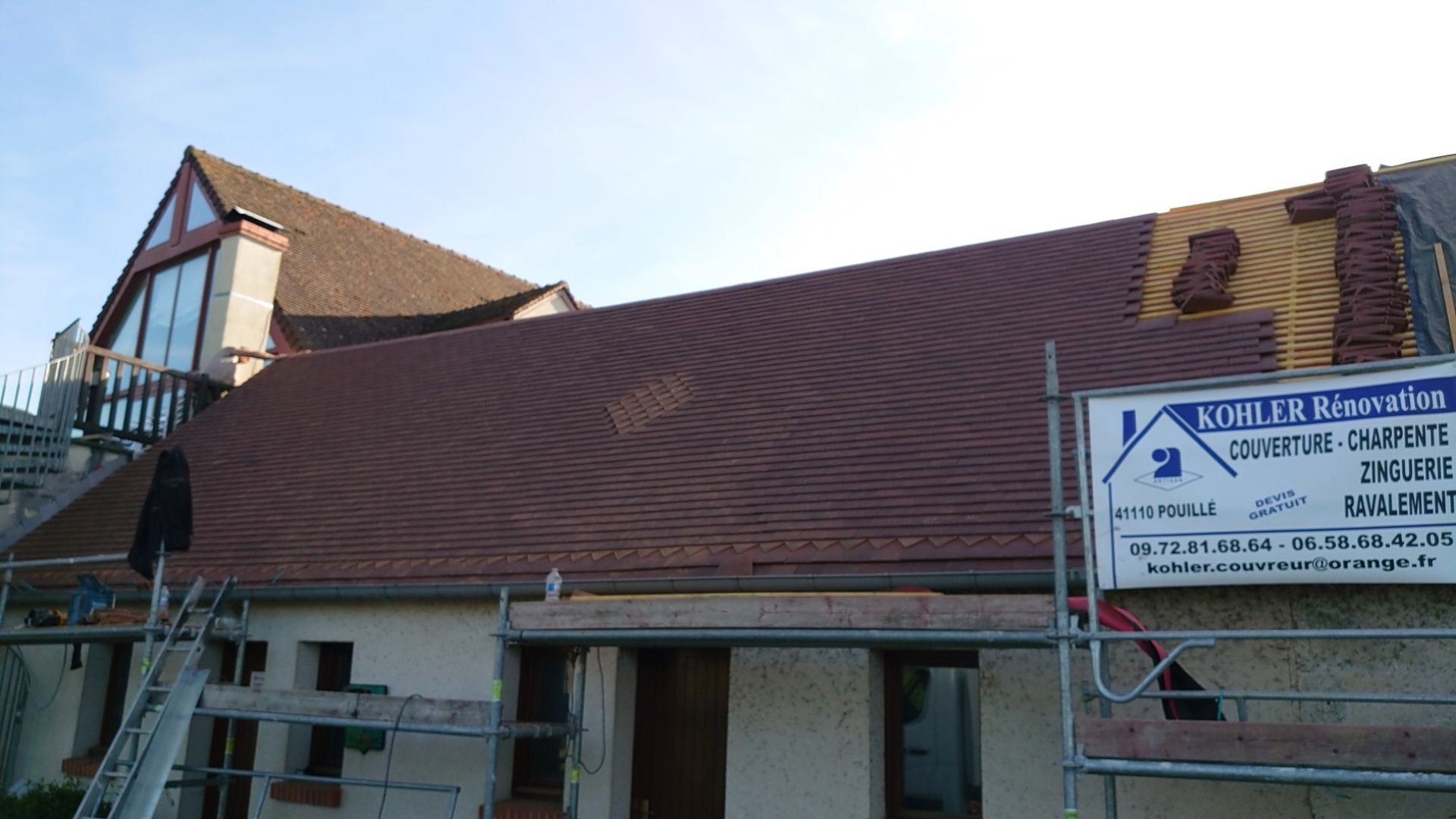 Un toit brun rougeâtre partiellement recouvert de tuiles, en cours de réparation, avec des échafaudages.