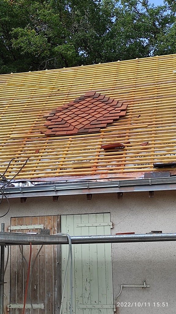 Une section de toiture en construction, montrant les lattes jaunes apparentes et une petite zone de tuiles en terre cuite rouges déjà posées.