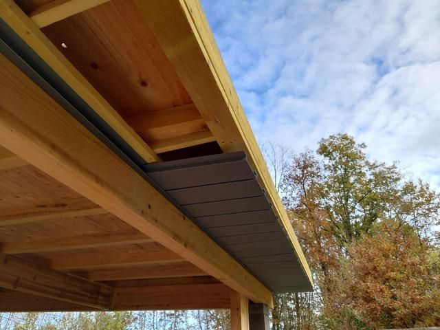 Face inférieure d'un auvent en bois avec un bardage gris foncé.