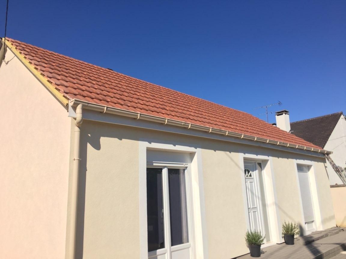 Maison beige avec un toit de tuiles rouges.