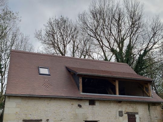 Maison en pierre avec un toit de tuiles récemment construit, une lucarne et des poutres en bois apparentes.