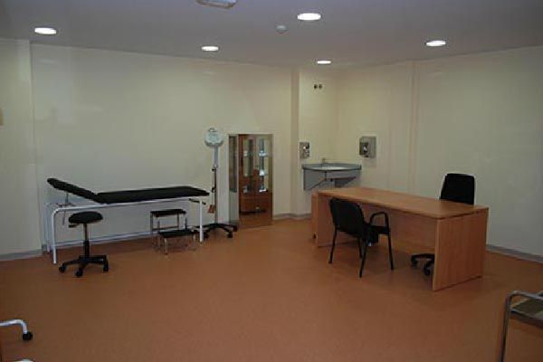 Un consultorio médico con un escritorio, sillas y una cama.