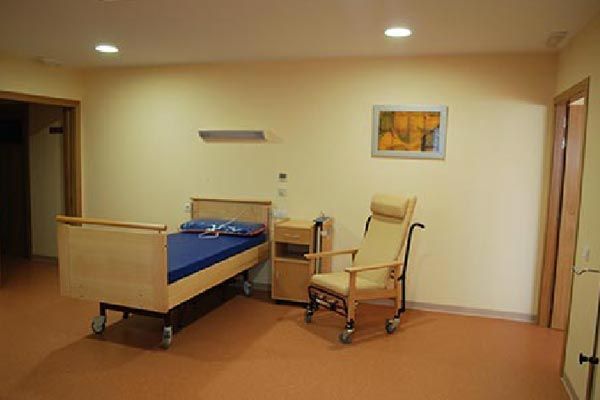 Una habitación de hospital con una cama, una silla y una mesita de noche.