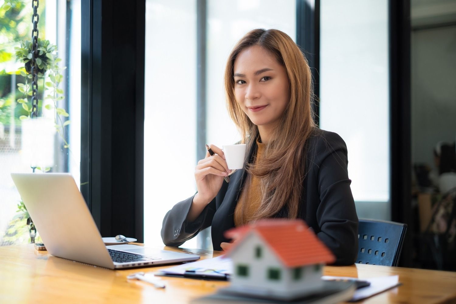 Una mujer está sentada en una mesa con una computadora portátil y una taza de café.
