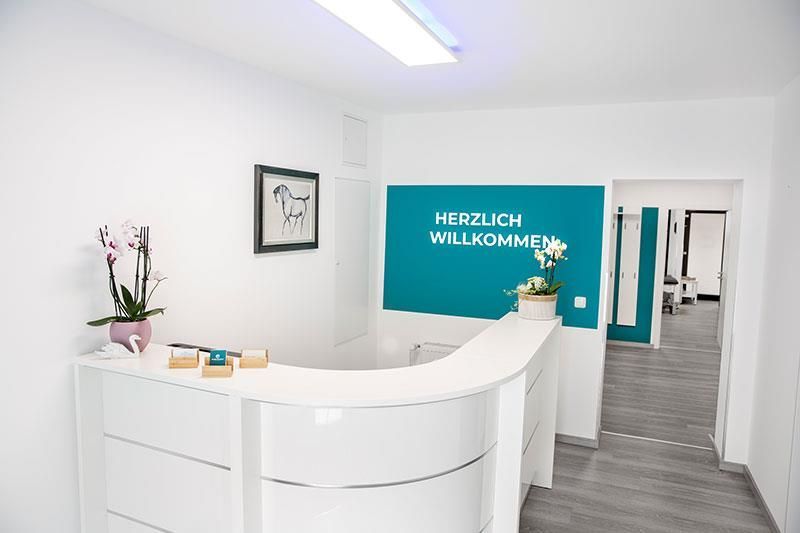 Ein weißer Rezeptionstresen mit einer blauen Wand mit der Aufschrift „Herzlich Willkommen“