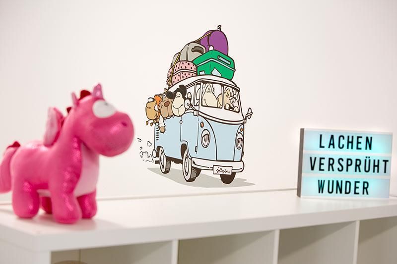Ein rosa Einhorn sitzt auf einem Regal neben einem Schild mit der Aufschrift „Lachen versprüht wunder“