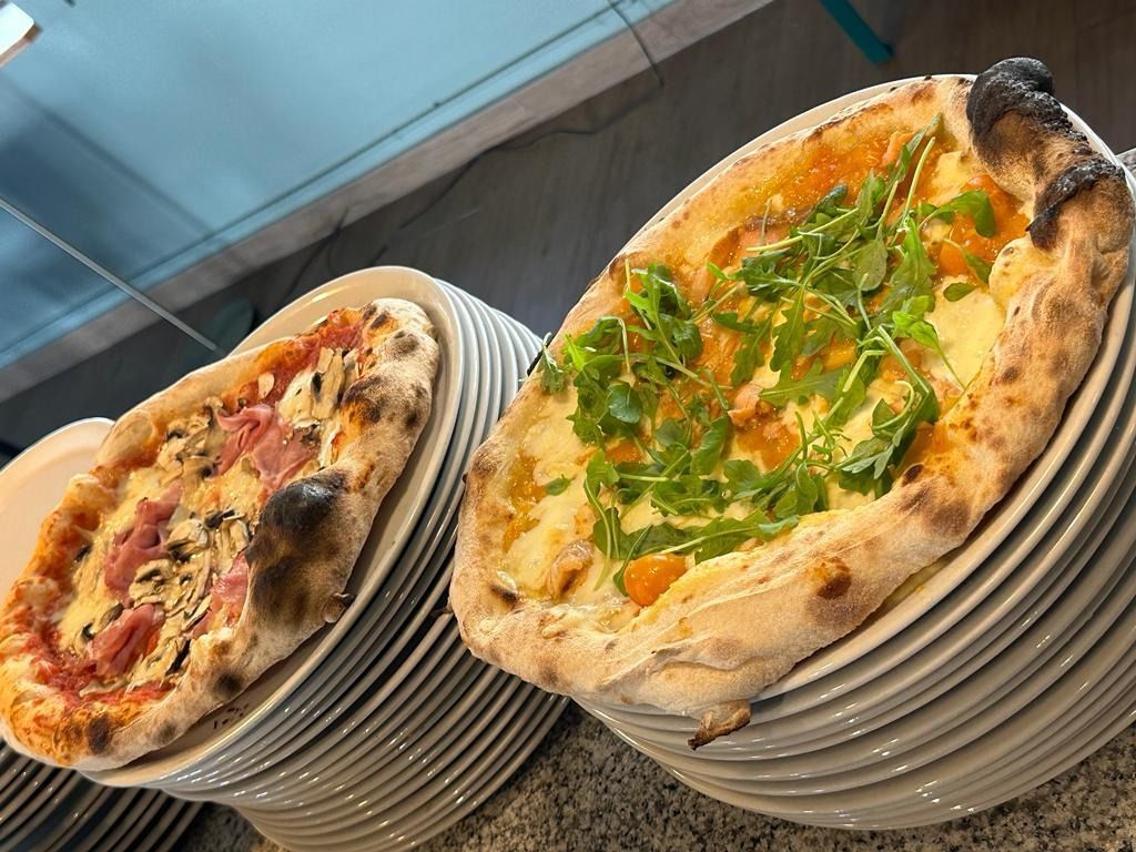 Hay dos pizzas sobre pilas de platos blancos sobre una mesa.