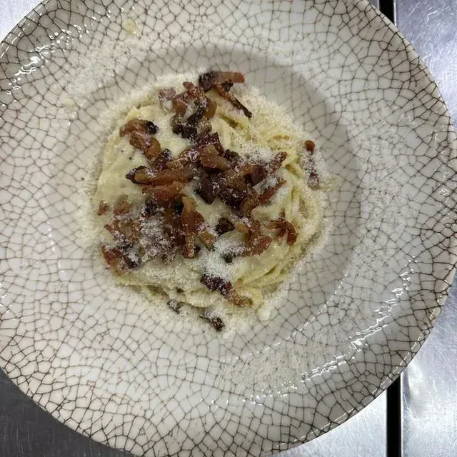 Un plato blanco cubierto con espaguetis y tocino sobre una mesa.