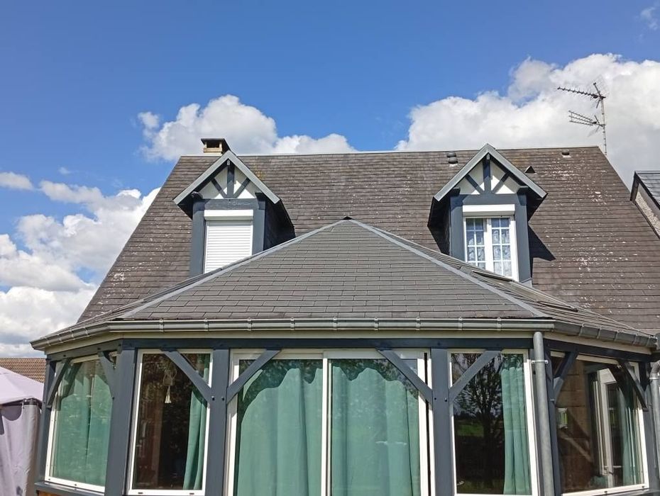 Extérieur de la maison avec toit gris, lucarnes et grandes fenêtres contre un ciel bleu.