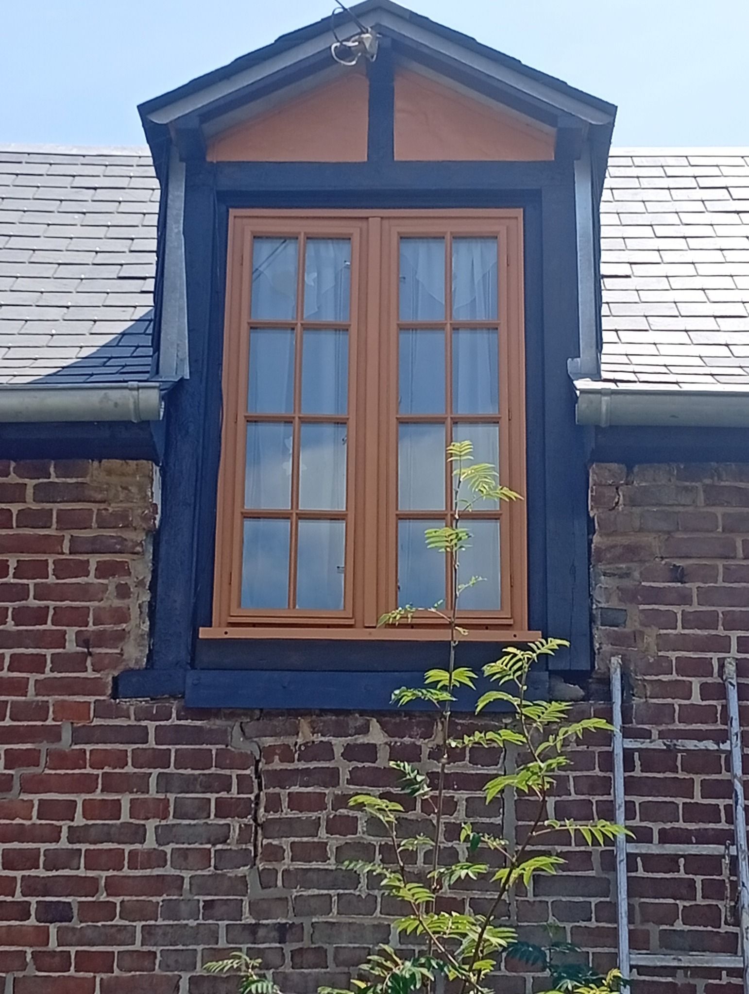Fenêtre avec cadre en bois clair et moulures foncées sur un mur en briques.