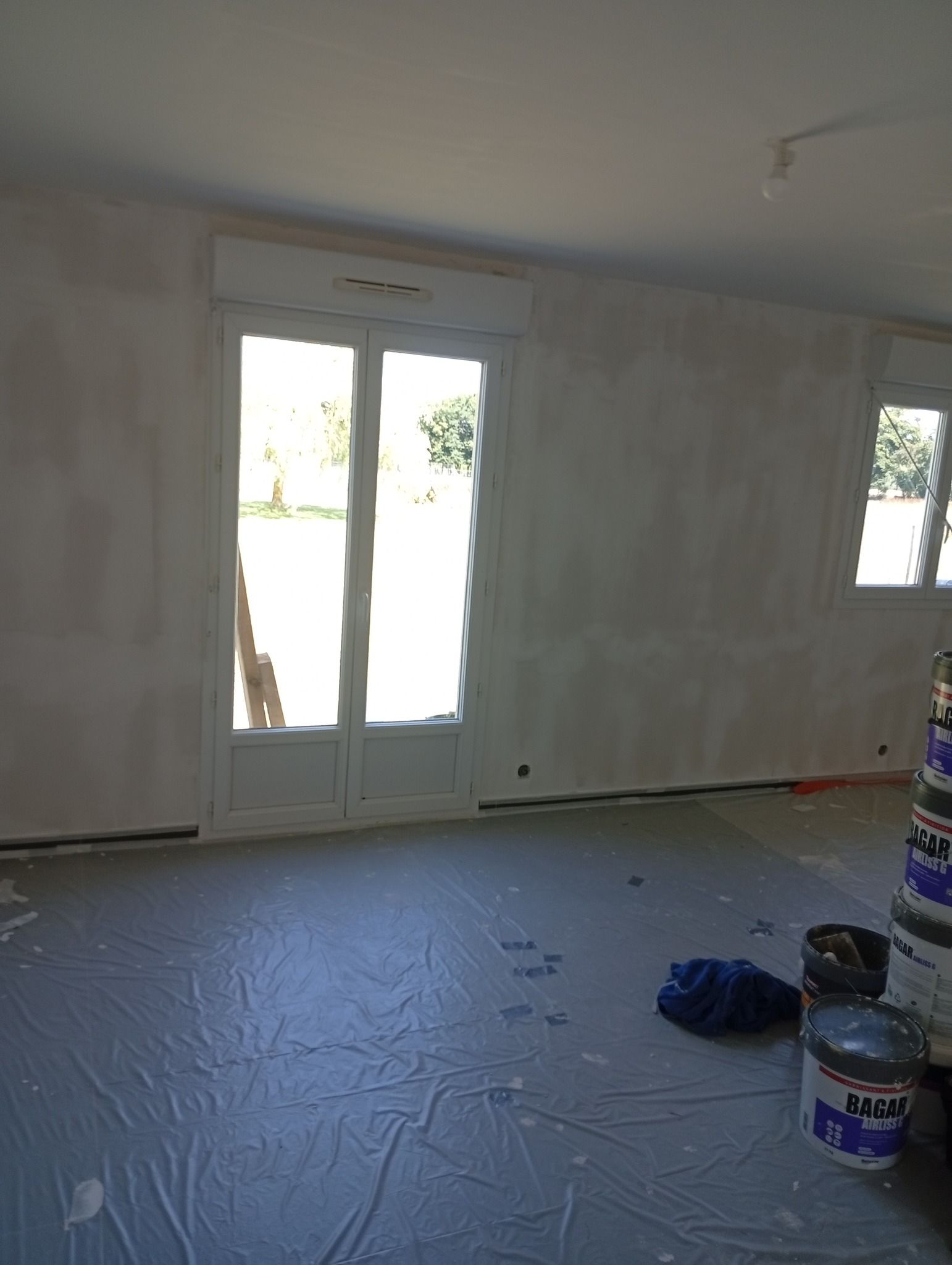 Pièce intérieure aux murs et à la porte blancs, prête à être peinte. Sol recouvert d'un film plastique de protection.