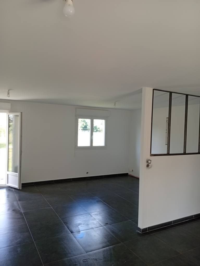 Pièce vide avec sol carrelé foncé, murs blancs et une fenêtre.