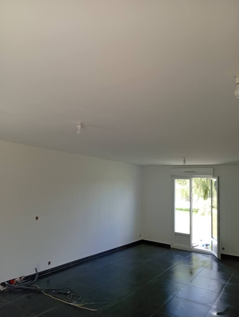 Pièce vide avec murs et plafond blancs, sol sombre et une porte vers l'extérieur.