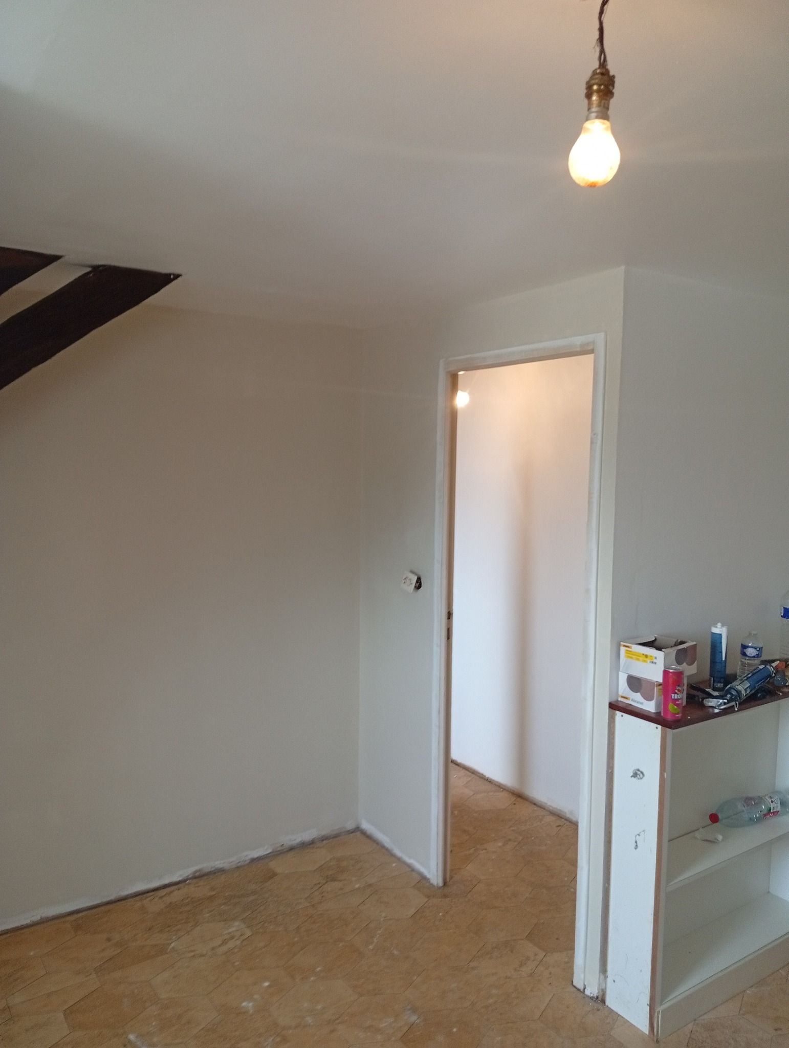 Une pièce avec des murs blancs, une porte, une ampoule et une petite étagère.