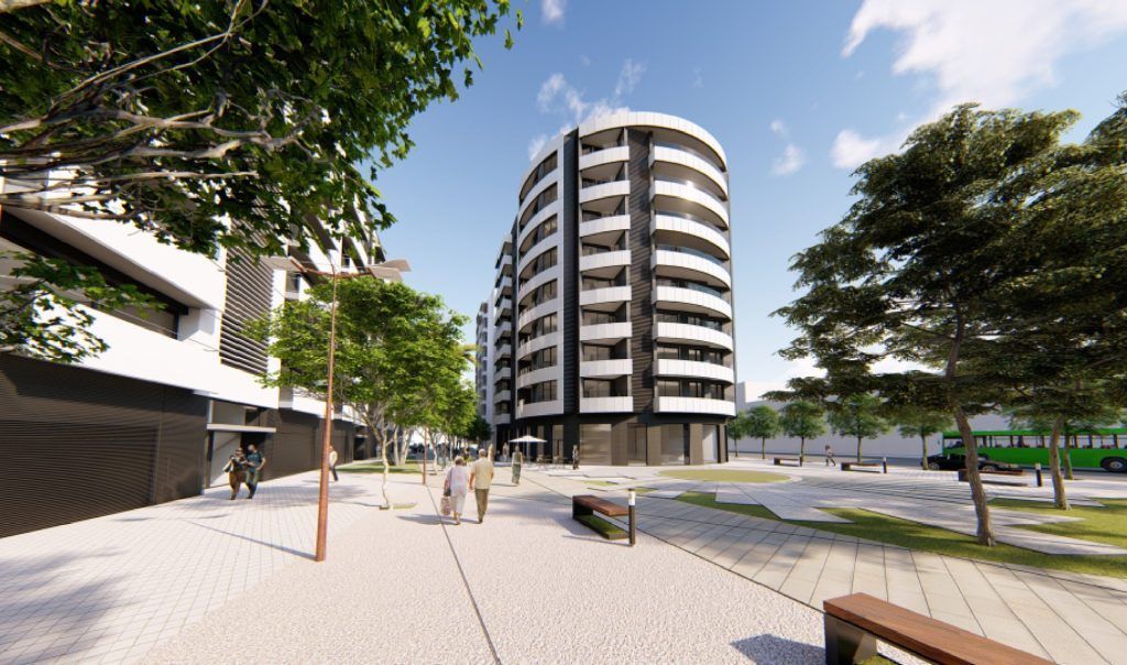 Un edificio de apartamentos moderno y curvo con balcones, cerca de una pasarela peatonal con árboles y bancos en un día soleado.