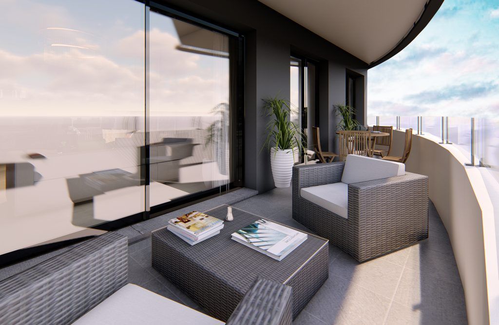 Balcón con muebles de mimbre gris, mesa de café con libros y plantas con vista a una vista nublada.