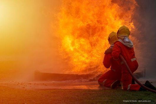 Feuerwehrleute in roten Schutzanzügen bekämpfen einen Großbrand mit Wasser.