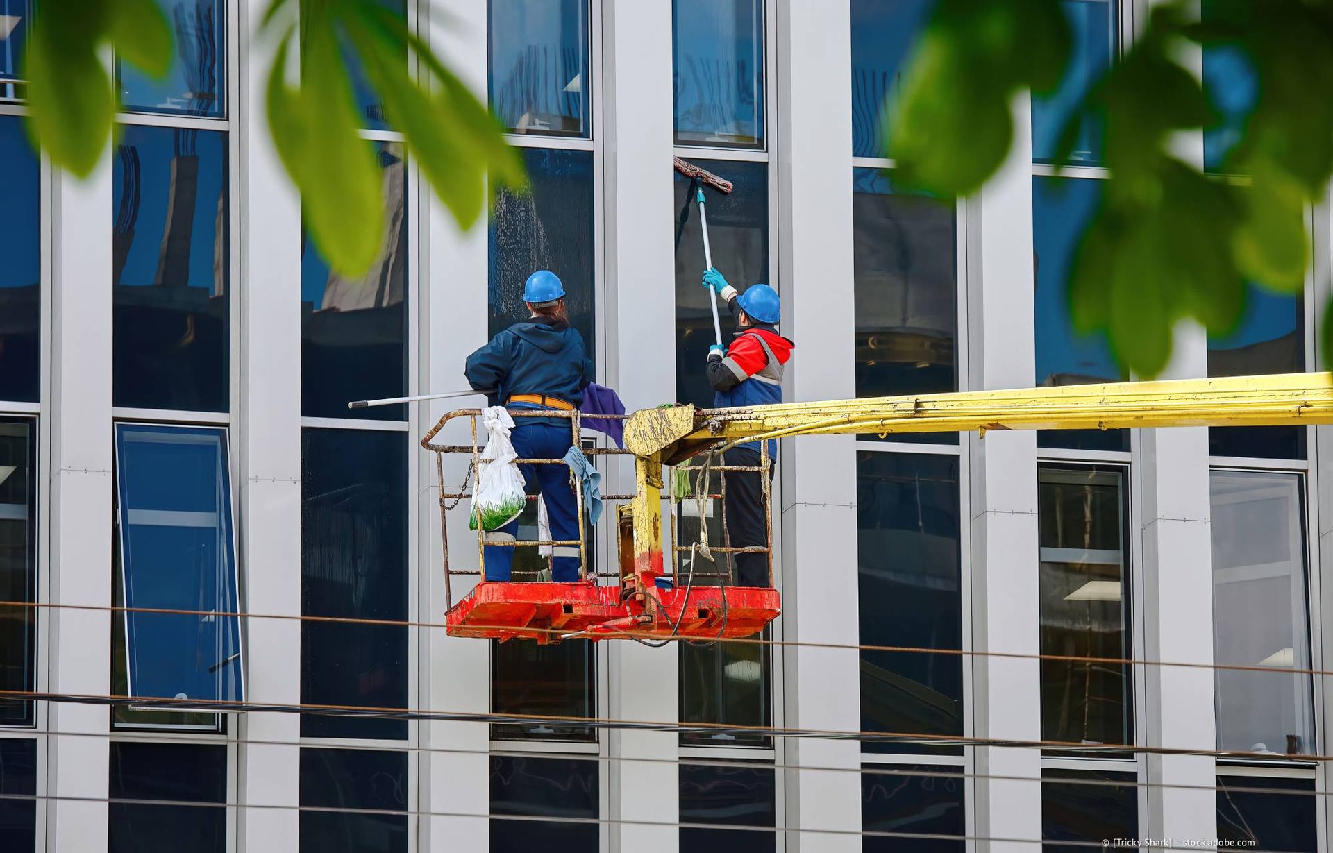 Zwei Fensterputzer reinigen mit einem Aufzug die Fenster eines hohen Gebäudes.