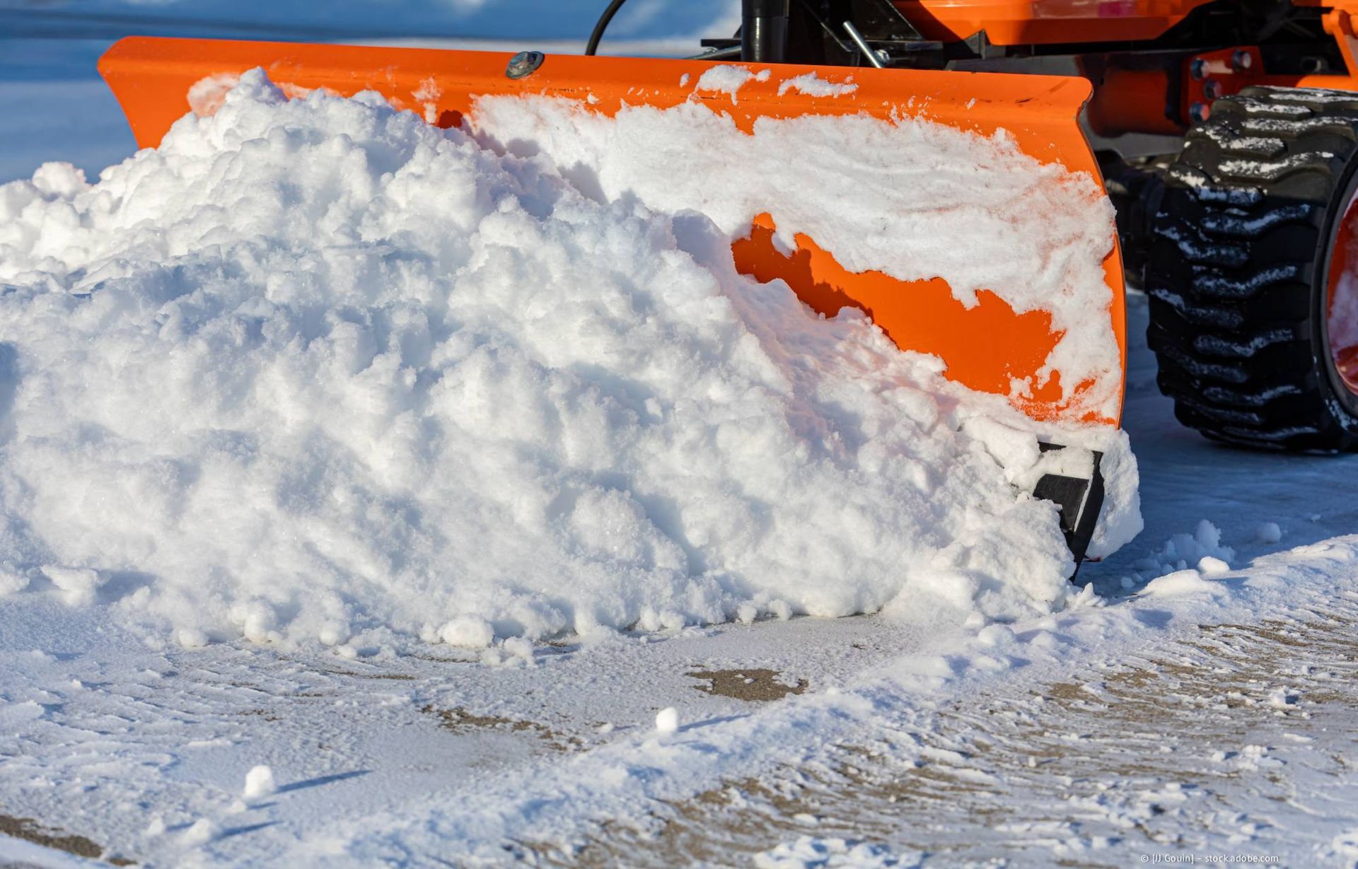 Ein orangefarbener Schneepflug schiebt einen großen Schneehaufen auf einer asphaltierten Fläche.