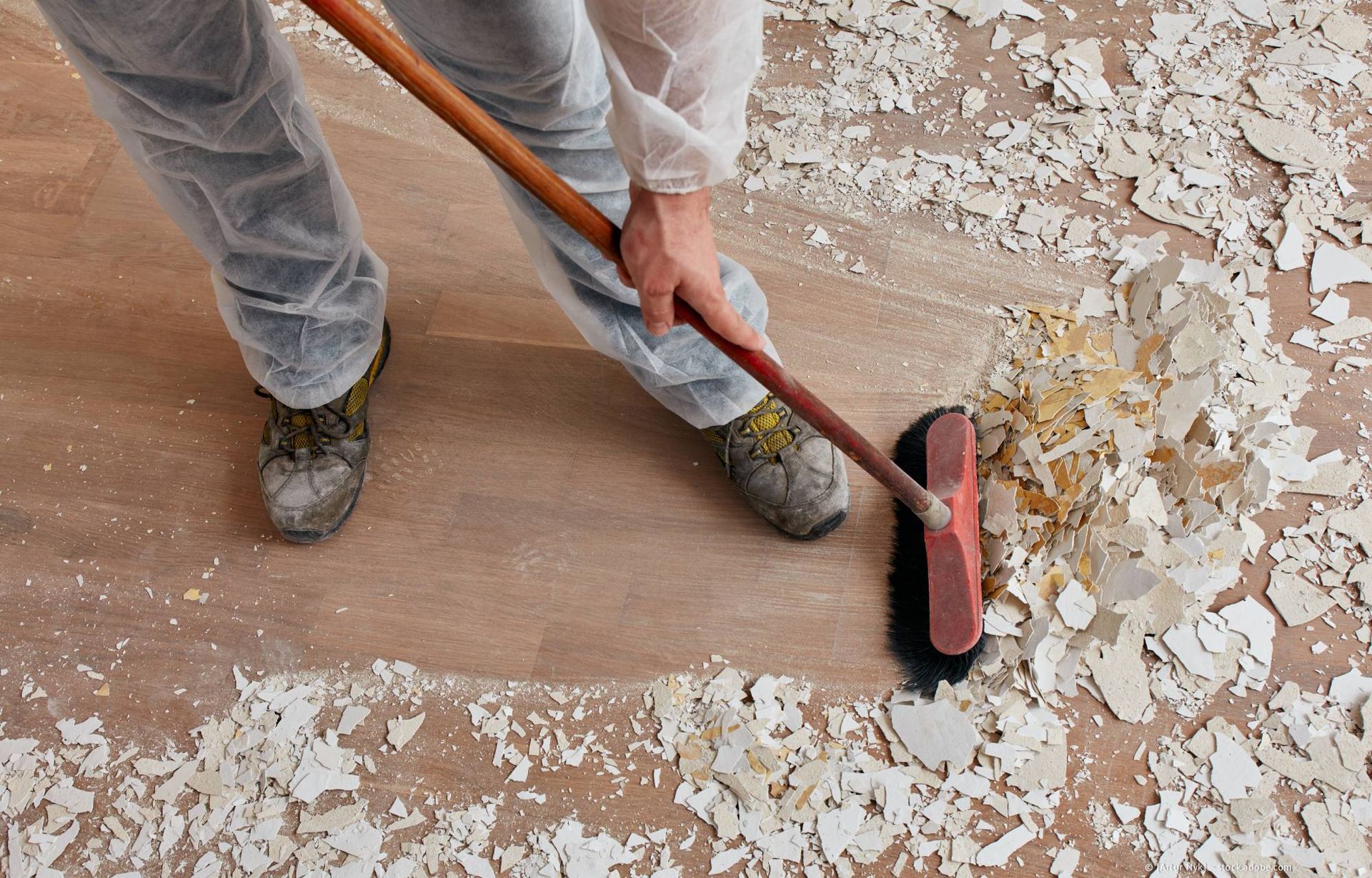 Eine Person in Schutzkleidung fegt Schutt von einem Holzboden.