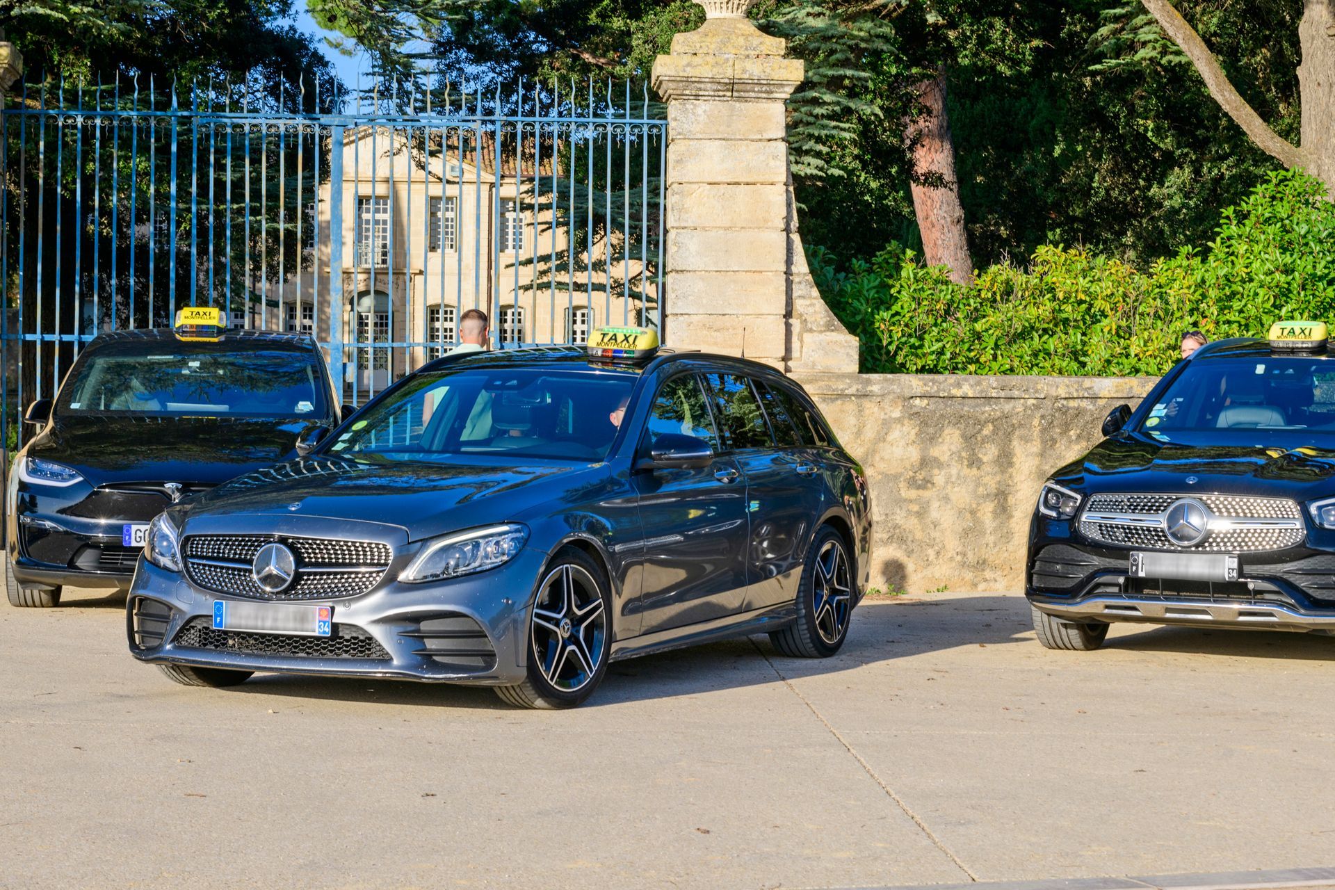 Deux Mercedes-AMG et une Tesla garées devant un portail 