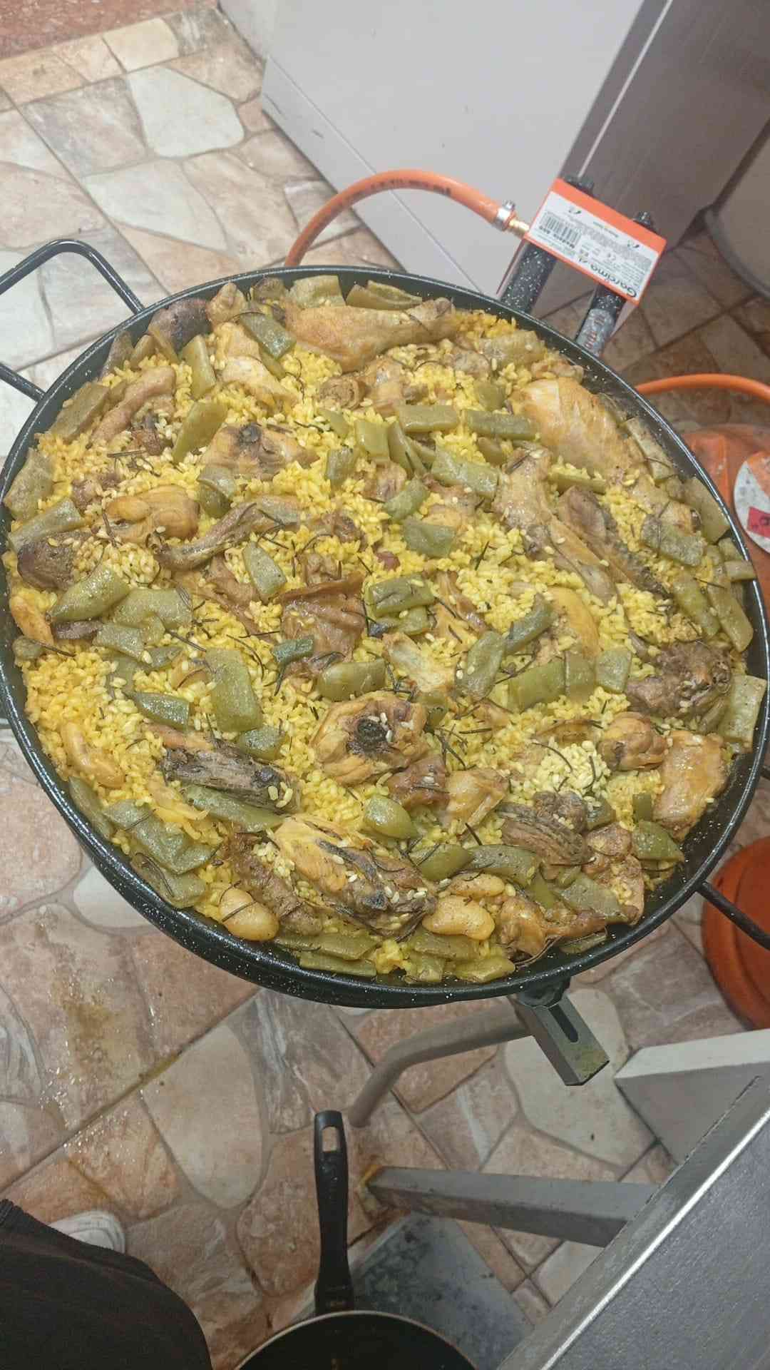 Paella grande con arroz, verduras y carne, cocinándose sobre llama de gas.