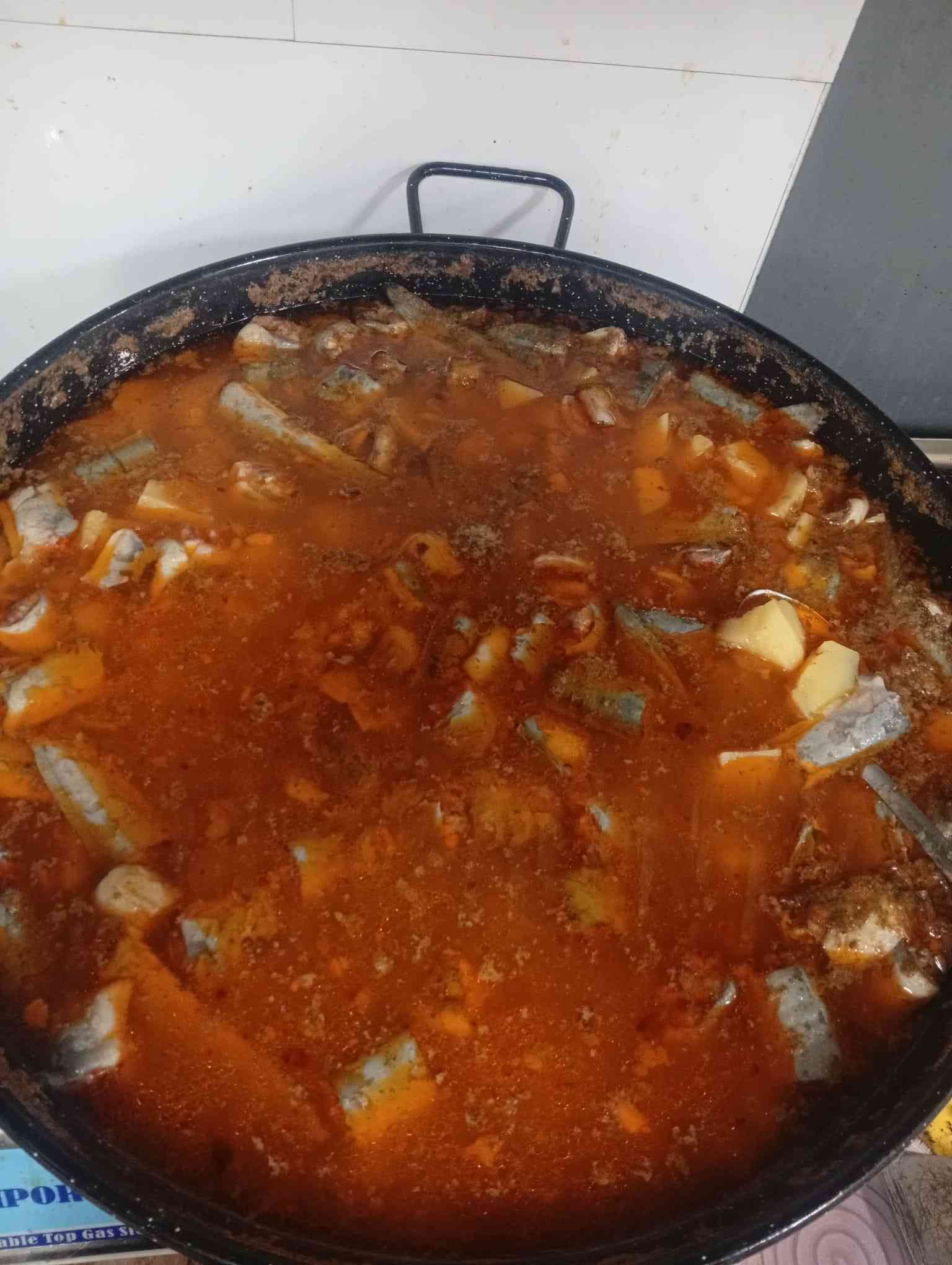 Cacerola grande y redonda llena de un guiso rojizo que contiene verduras y trozos de carne.