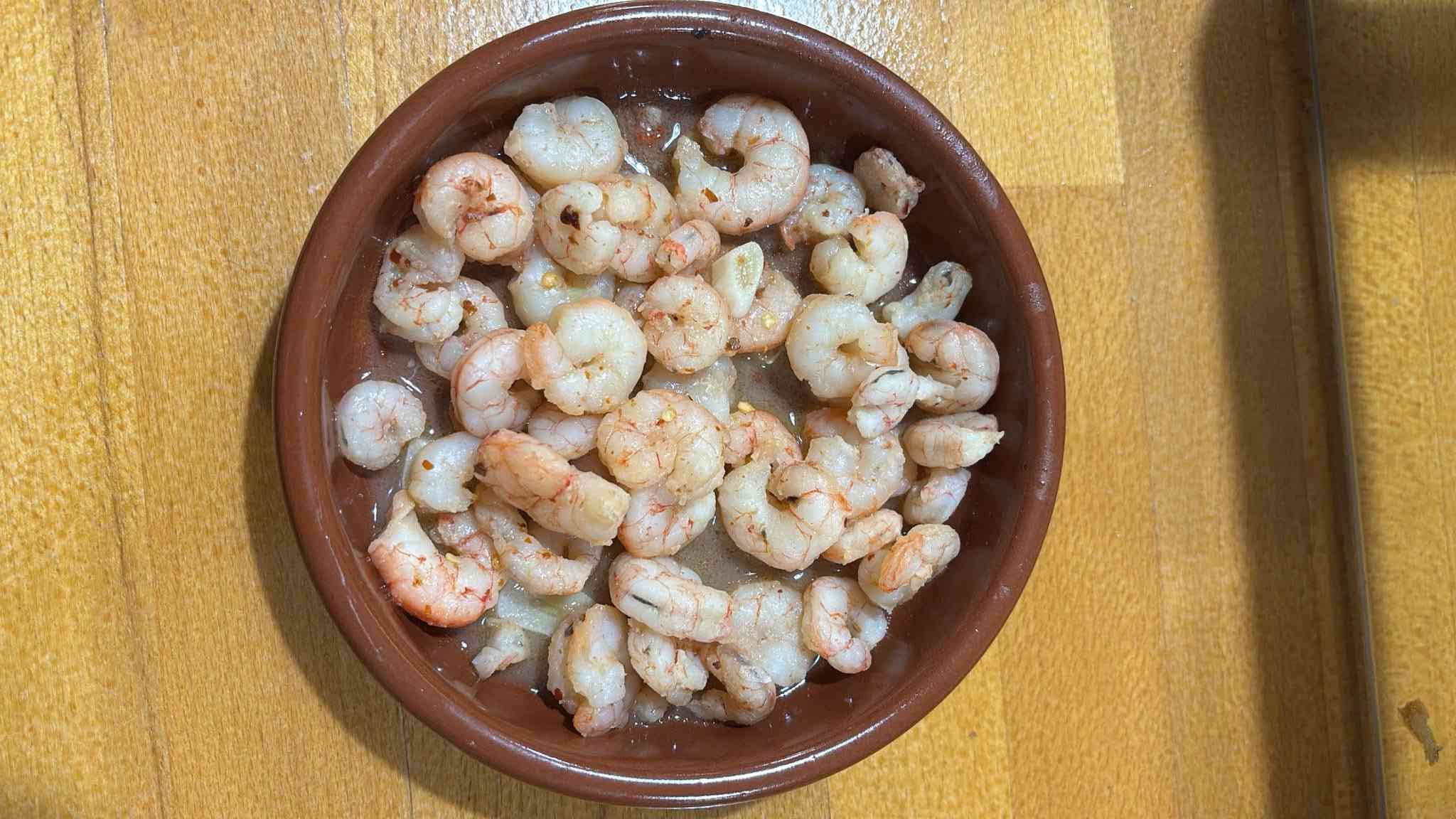 Camarones cocidos en un recipiente marrón, espolvoreados con condimentos, sobre una superficie de madera.