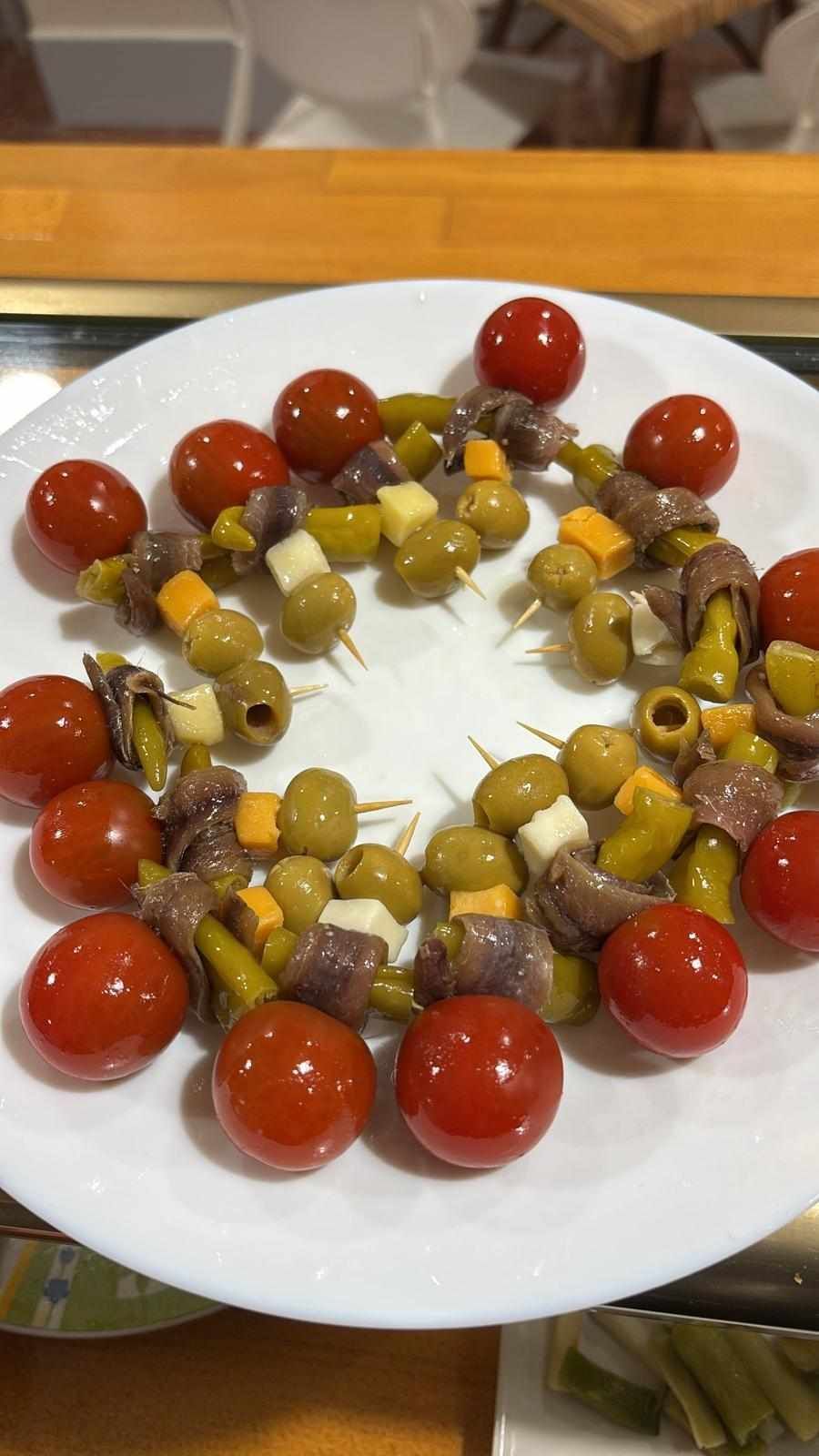 Plato de entrantes: aceitunas, tomates, anchoas, queso y pimientos en brochetas.
