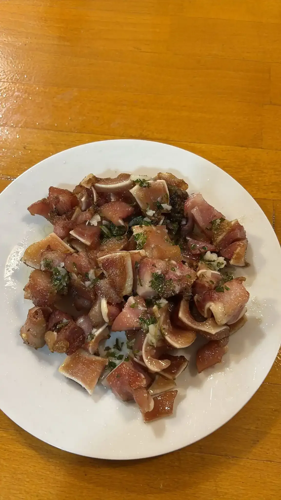 Orejas de cerdo picadas en un plato blanco, condimentadas con hierbas, sobre una mesa de madera.