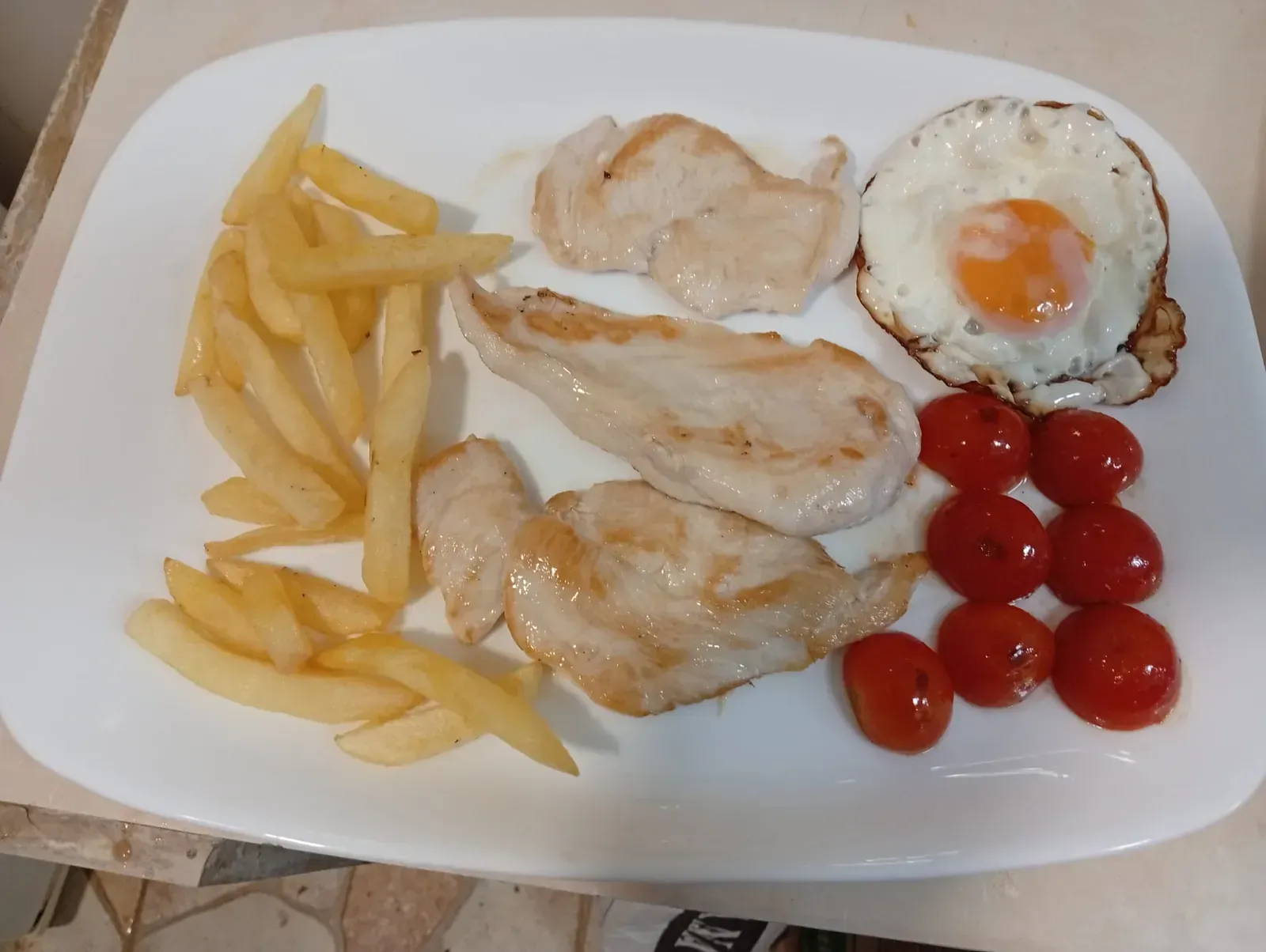 Plato con pollo, patatas fritas, huevo frito y tomates.