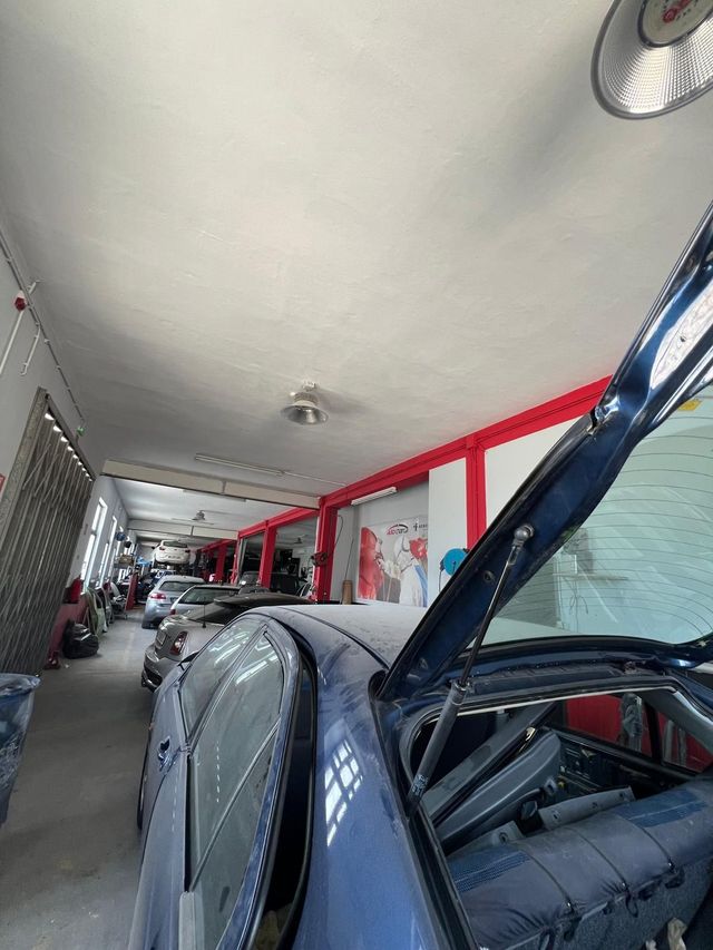 Um carro azul-escuro com o capô aberto dentro de uma garagem. Outros carros enfileiram-se nas paredes.