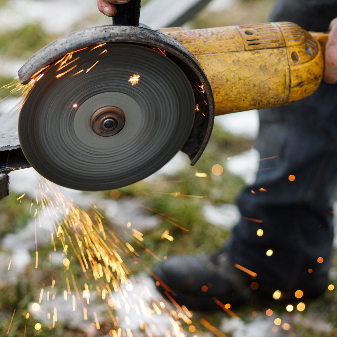 Une personne utilise une meuleuse d'angle jaune, créant des étincelles tout en coupant du métal à l'extérieur.