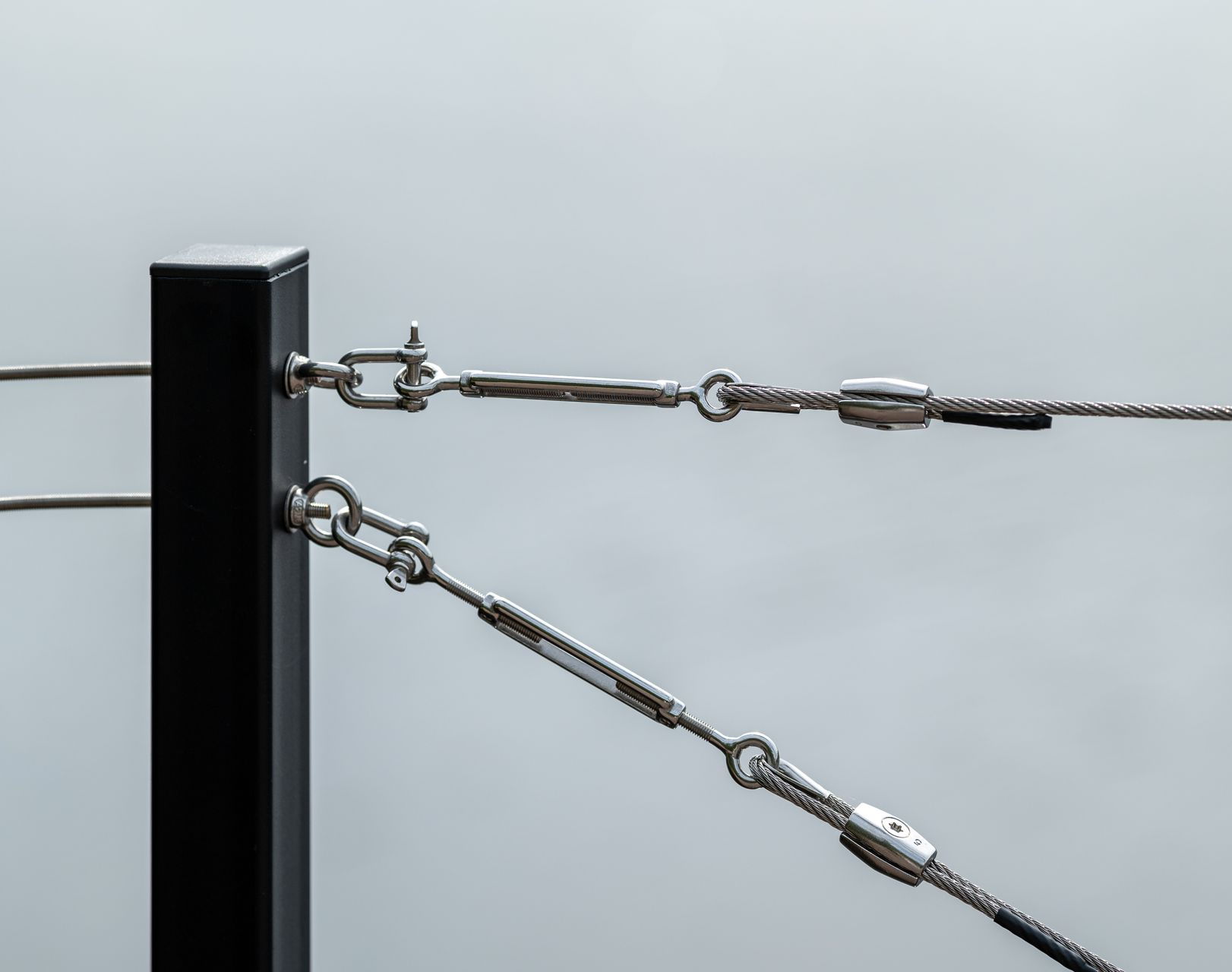 Poteau en métal noir avec deux garde-corps horizontaux en câble d'acier en inox et tendeurs.