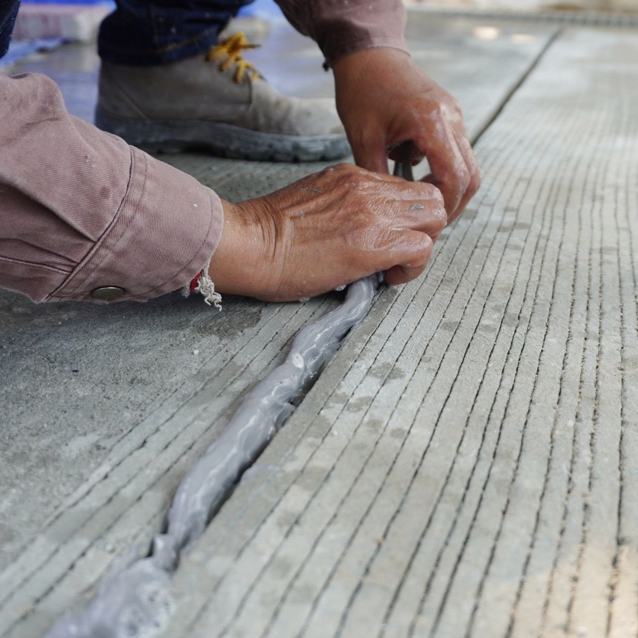 Personne appliquant à la main du mastic sur un joint de sol en béton.