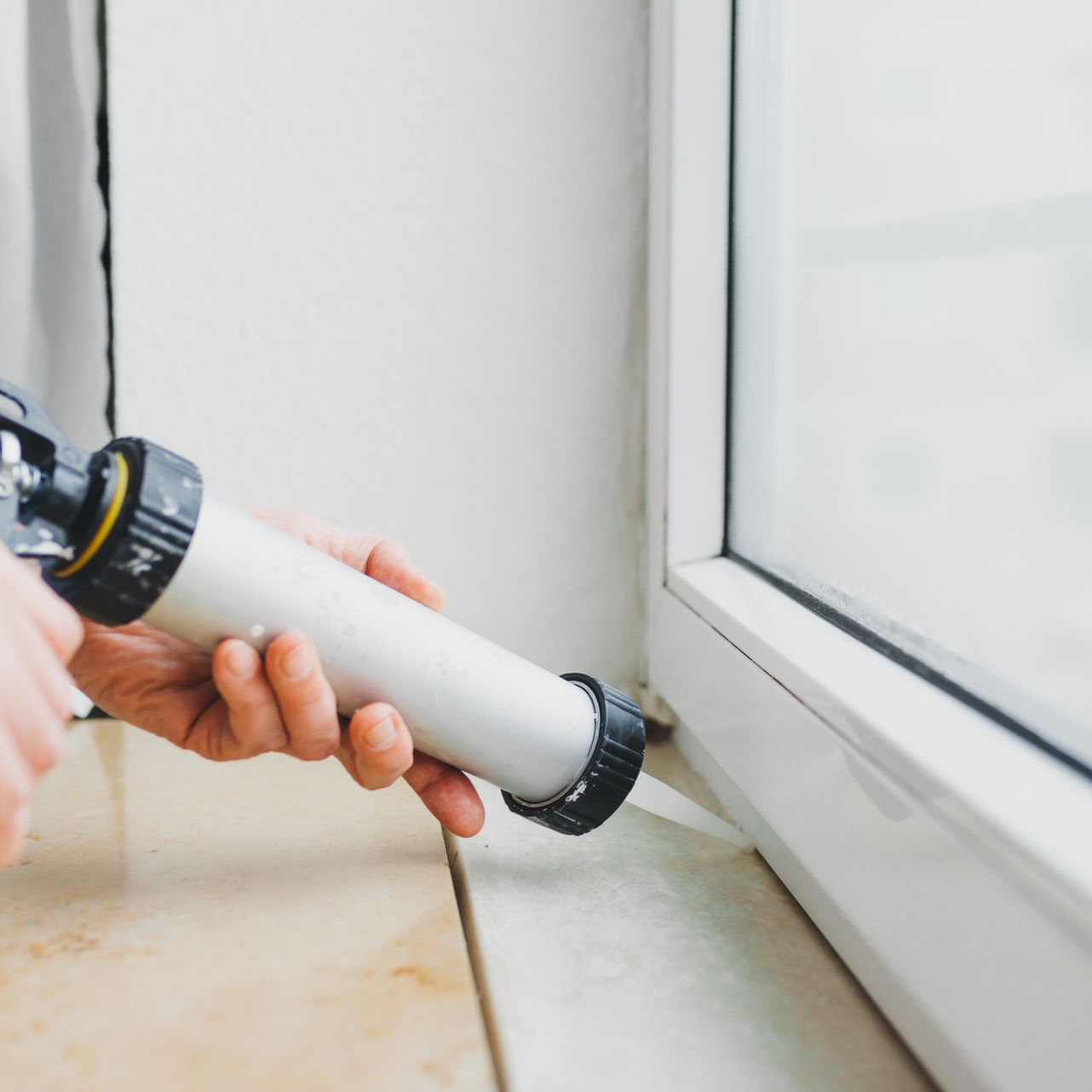Personne appliquant du mastic sur un cadre de fenêtre à l'aide d'un pistolet.