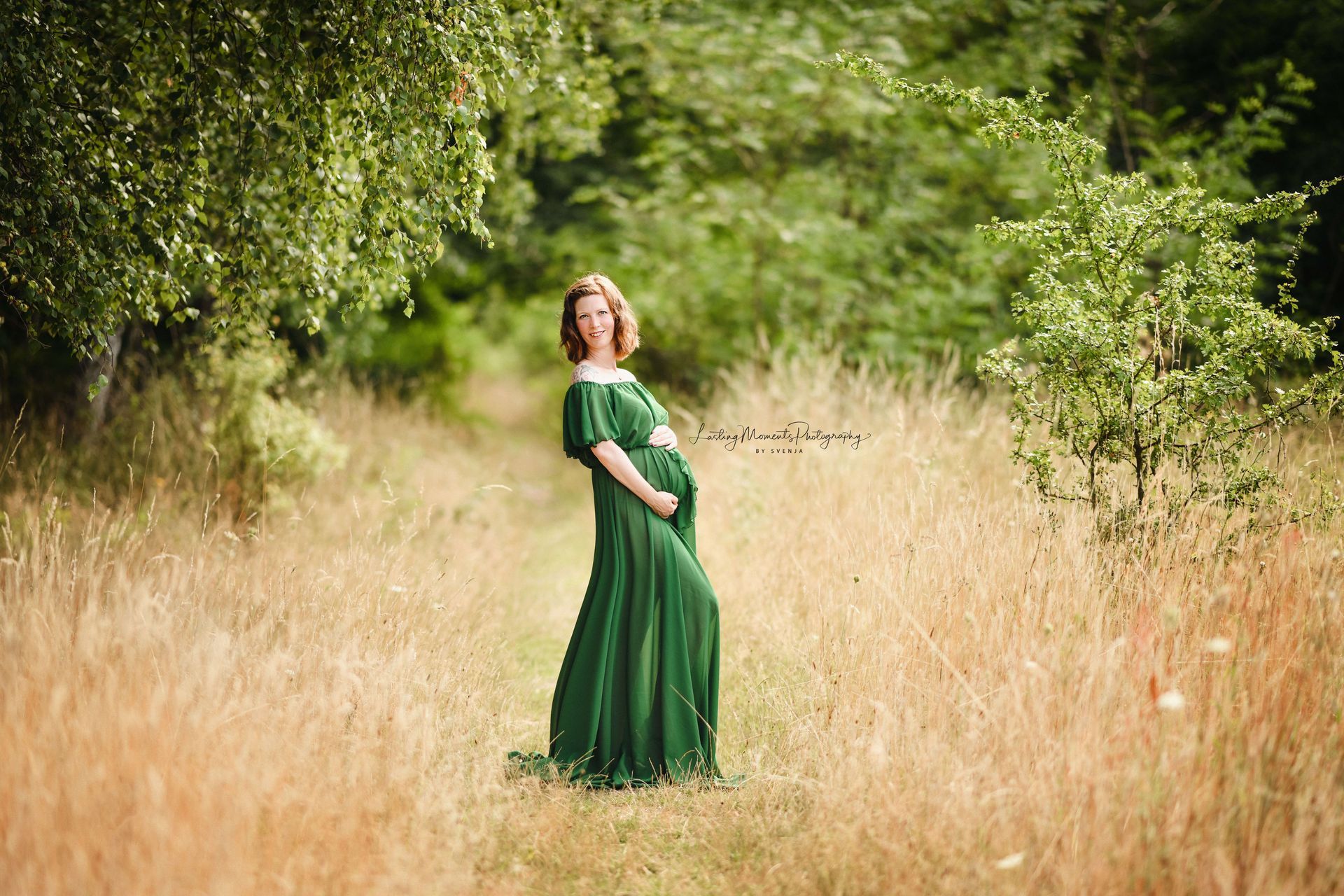 Eine schwangere Frau in einem grünen Kleid steht auf einem Feld.
