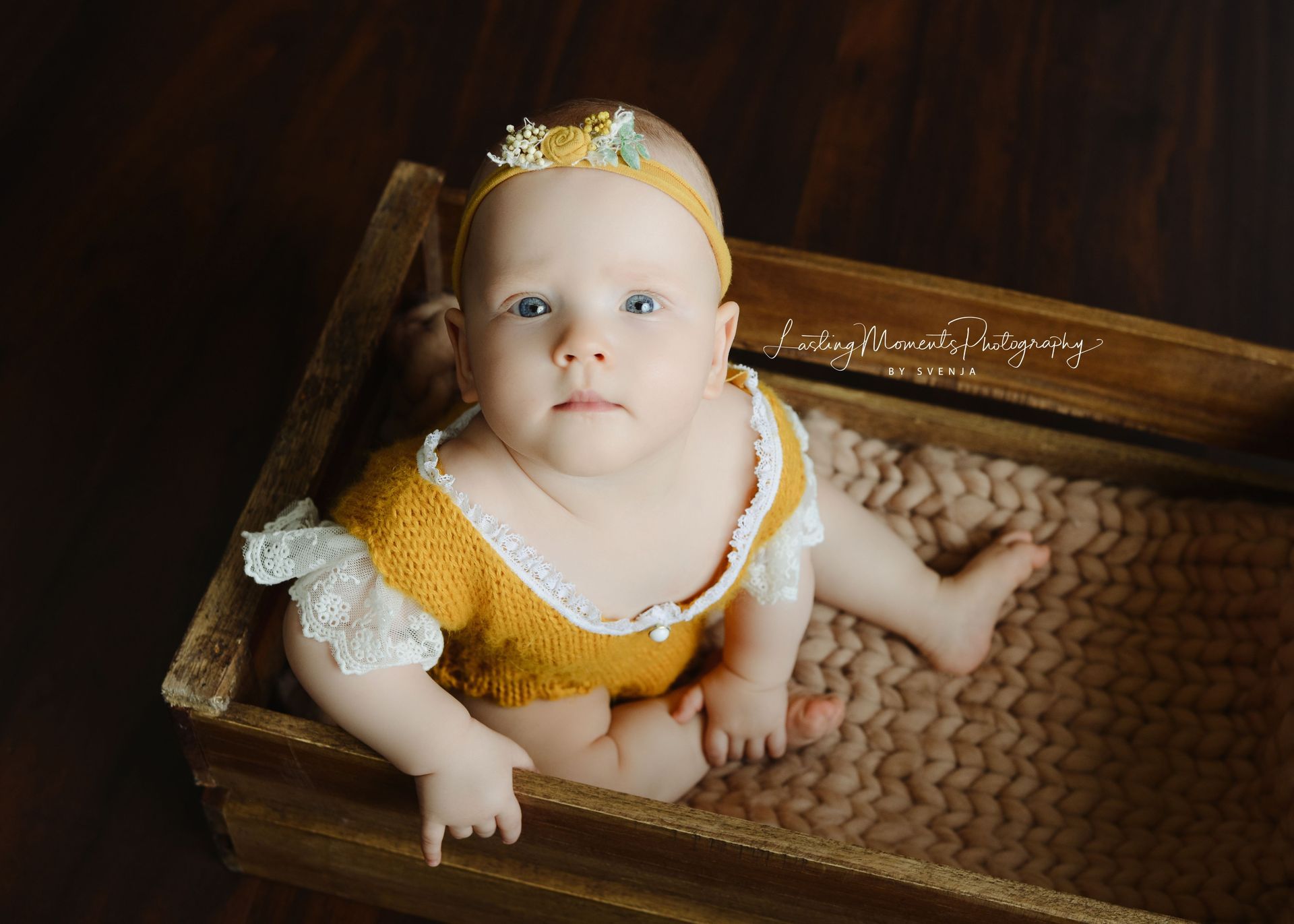 Ein Baby in einem gelben Outfit sitzt in einer Holzkiste.
