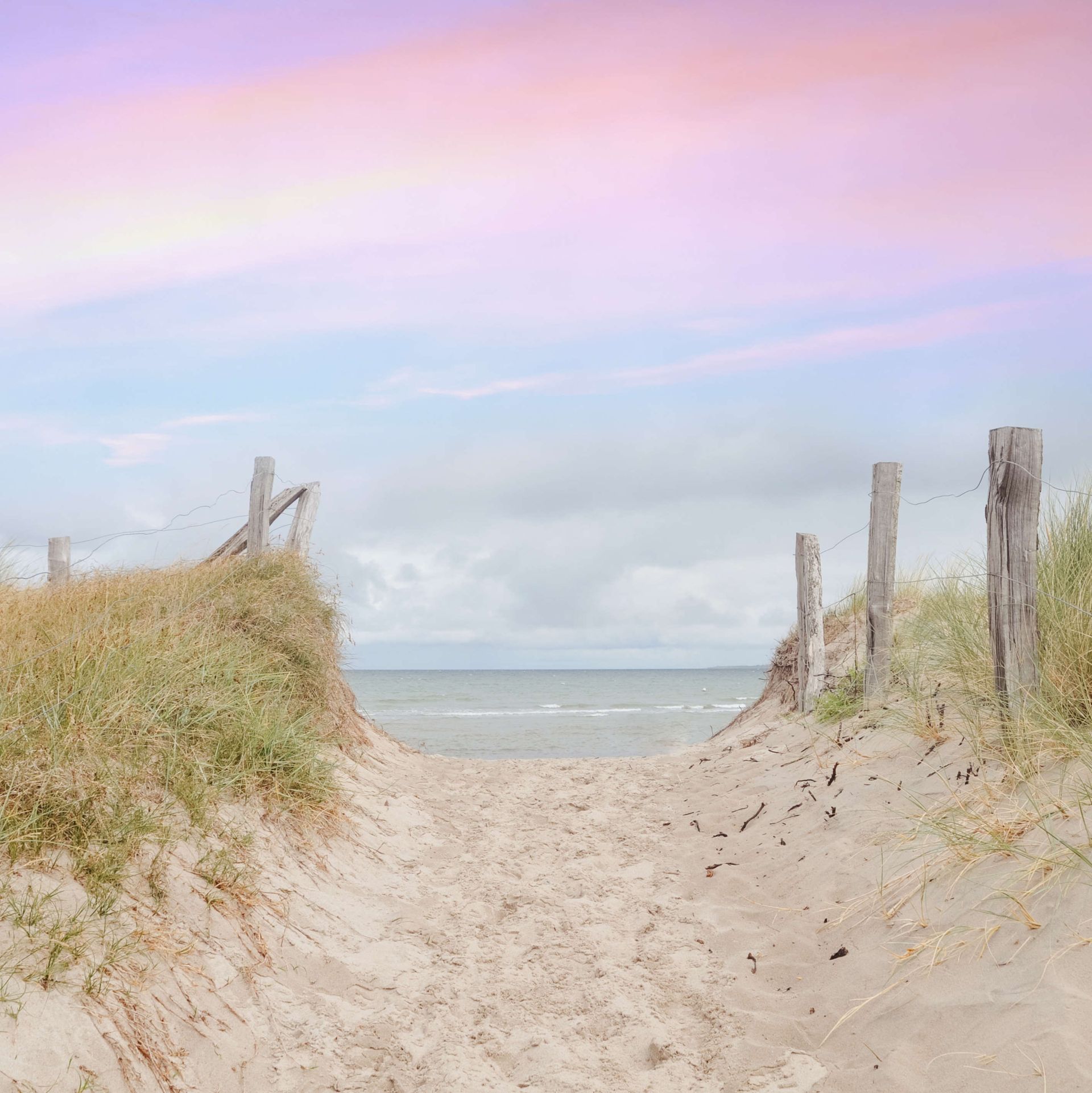 Ein Sandweg, der zum Meer führt, mit einem rosa Himmel im Hintergrund