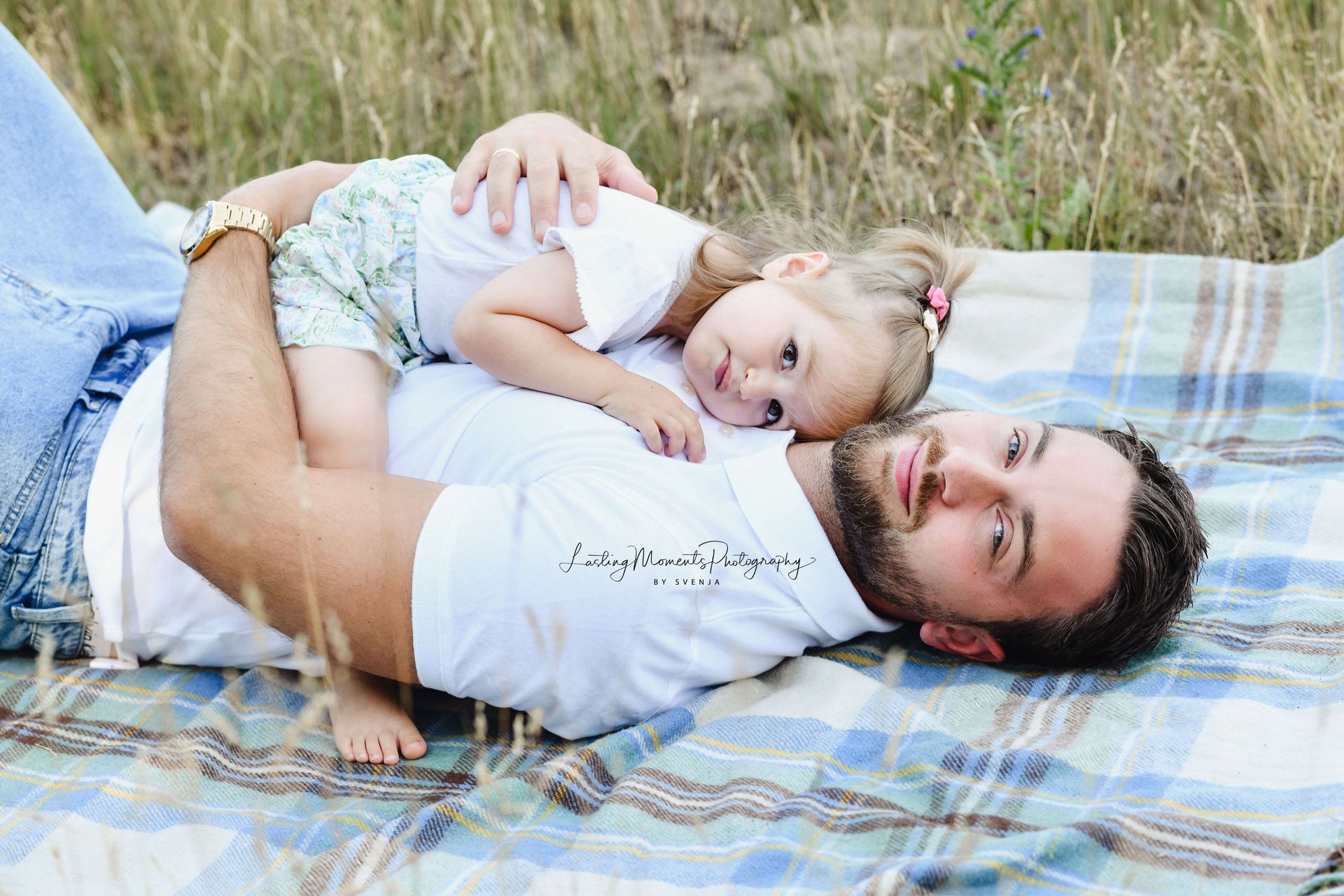 Ein Mann liegt auf einer Decke und hält ein kleines Mädchen.