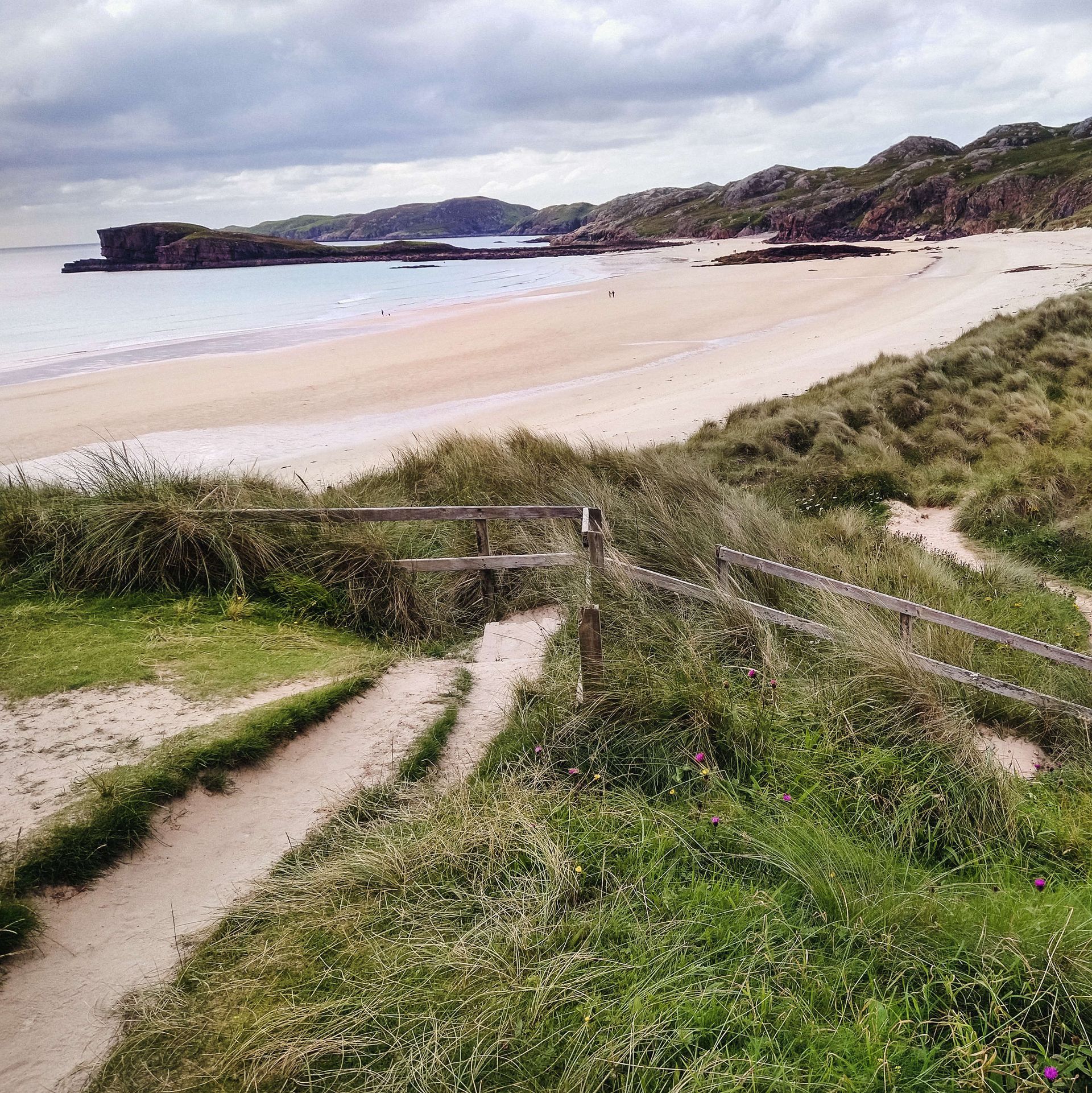 Ein Weg, der zu einem Strand führt, mit einem Zaun im Vordergrund