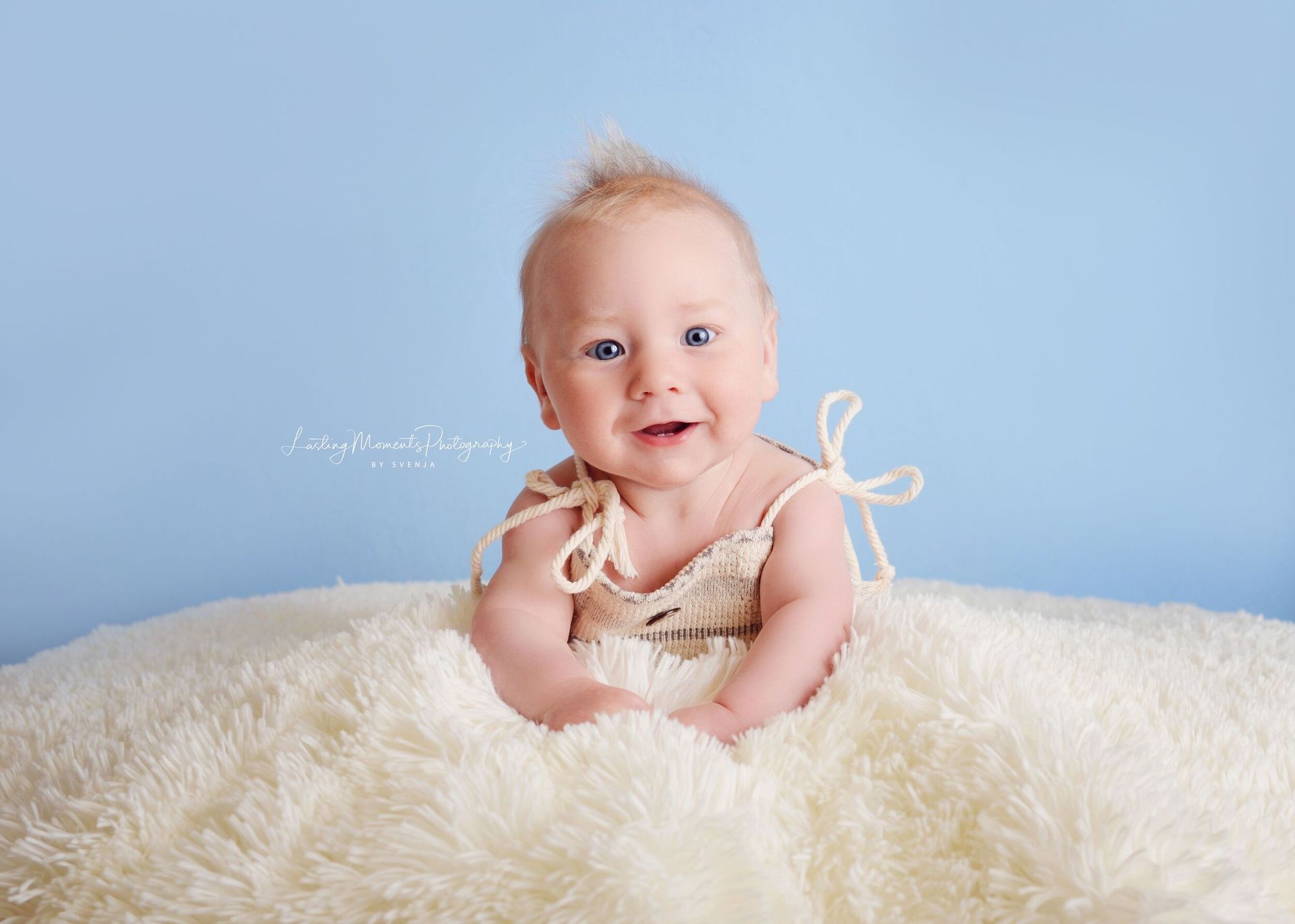 Ein Baby liegt auf einer weißen Decke und lächelt.