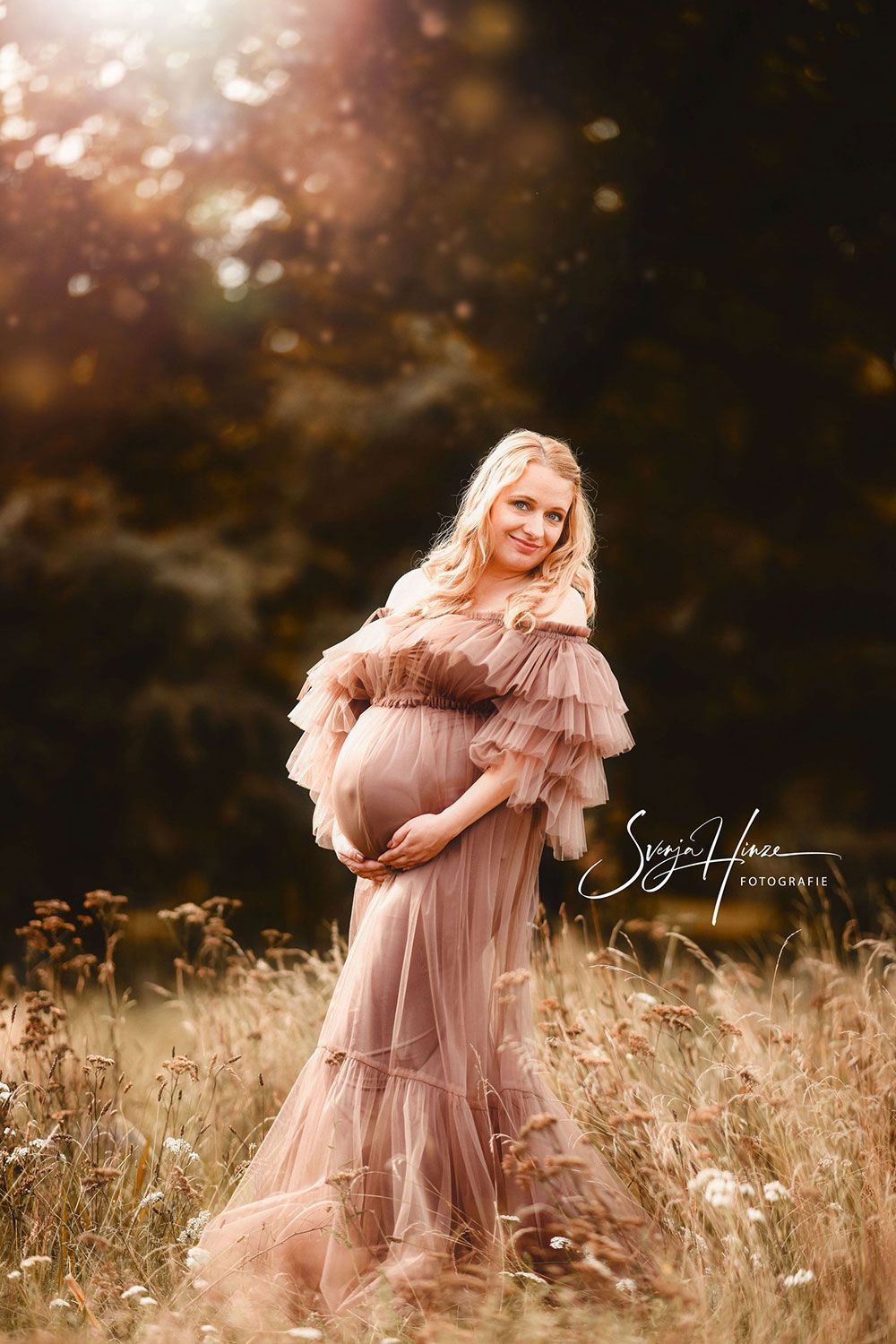 Eine schwangere Frau steht auf einem Feld und hält ihren Bauch.