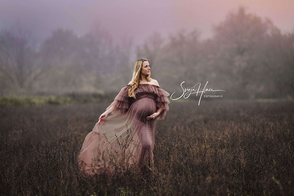 Eine schwangere Frau in einem langen Kleid steht auf einem Feld.