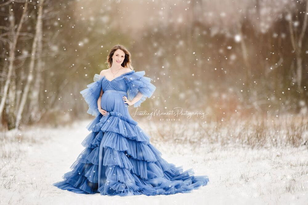 Eine schwangere Frau in einem blauen Kleid steht im Schnee.