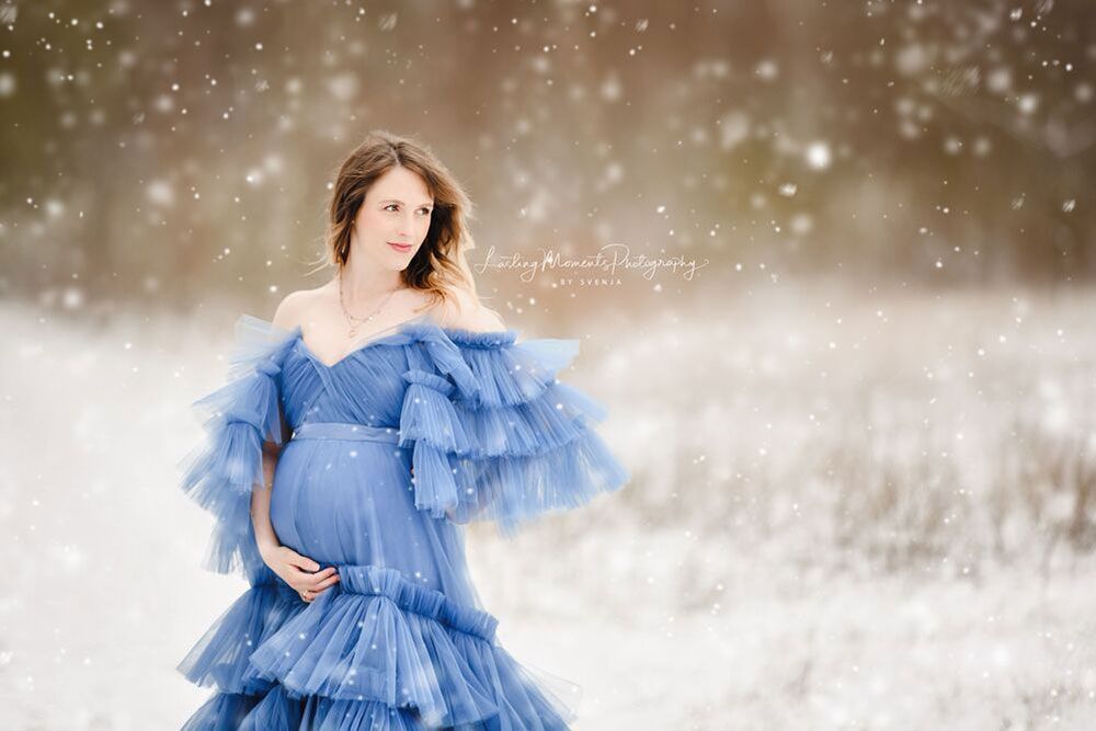 Eine schwangere Frau in einem blauen Kleid steht im Schnee.
