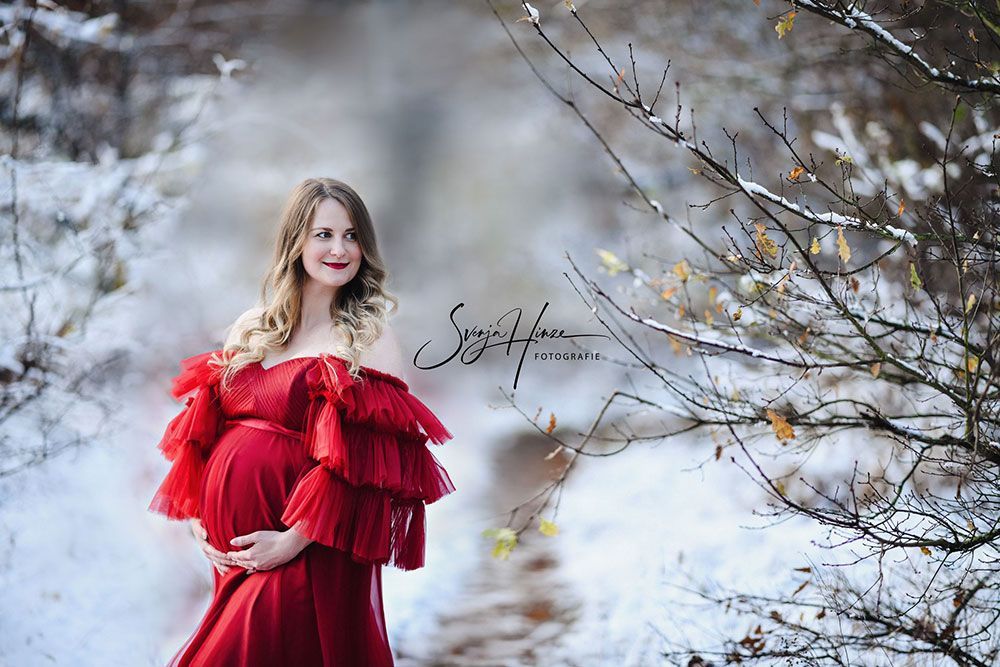Eine schwangere Frau in einem roten Kleid steht im Schnee.